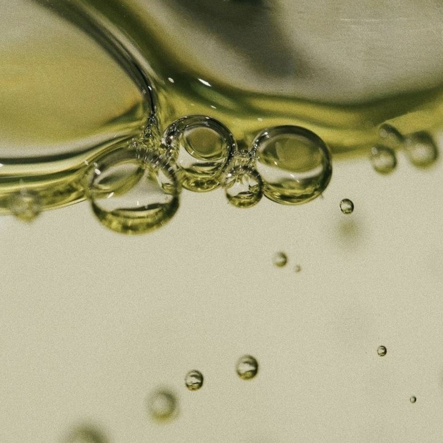 A close-up image showing oil drops with a transparent, glossy appearance, capturing the intricate details of droplets resting on a surface. The drops vary in size and reflect light, showcasing their fluid nature and moisture content.