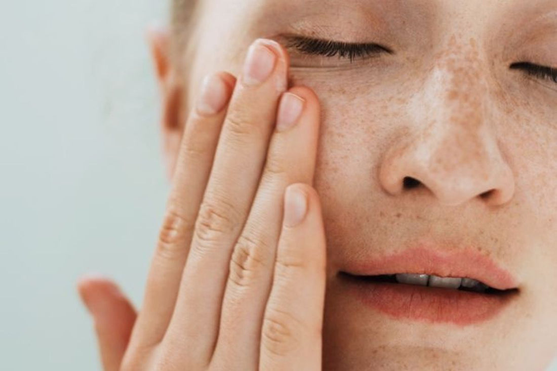 A close up of a woman touching her skin with her hand.
