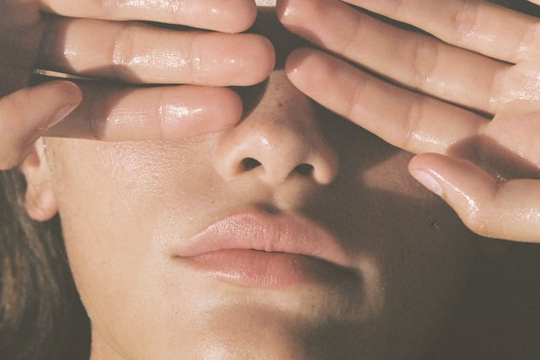 Woman with dewy skin gently shielding her face with her hands, illustrating sensitivity to light and delicate skin