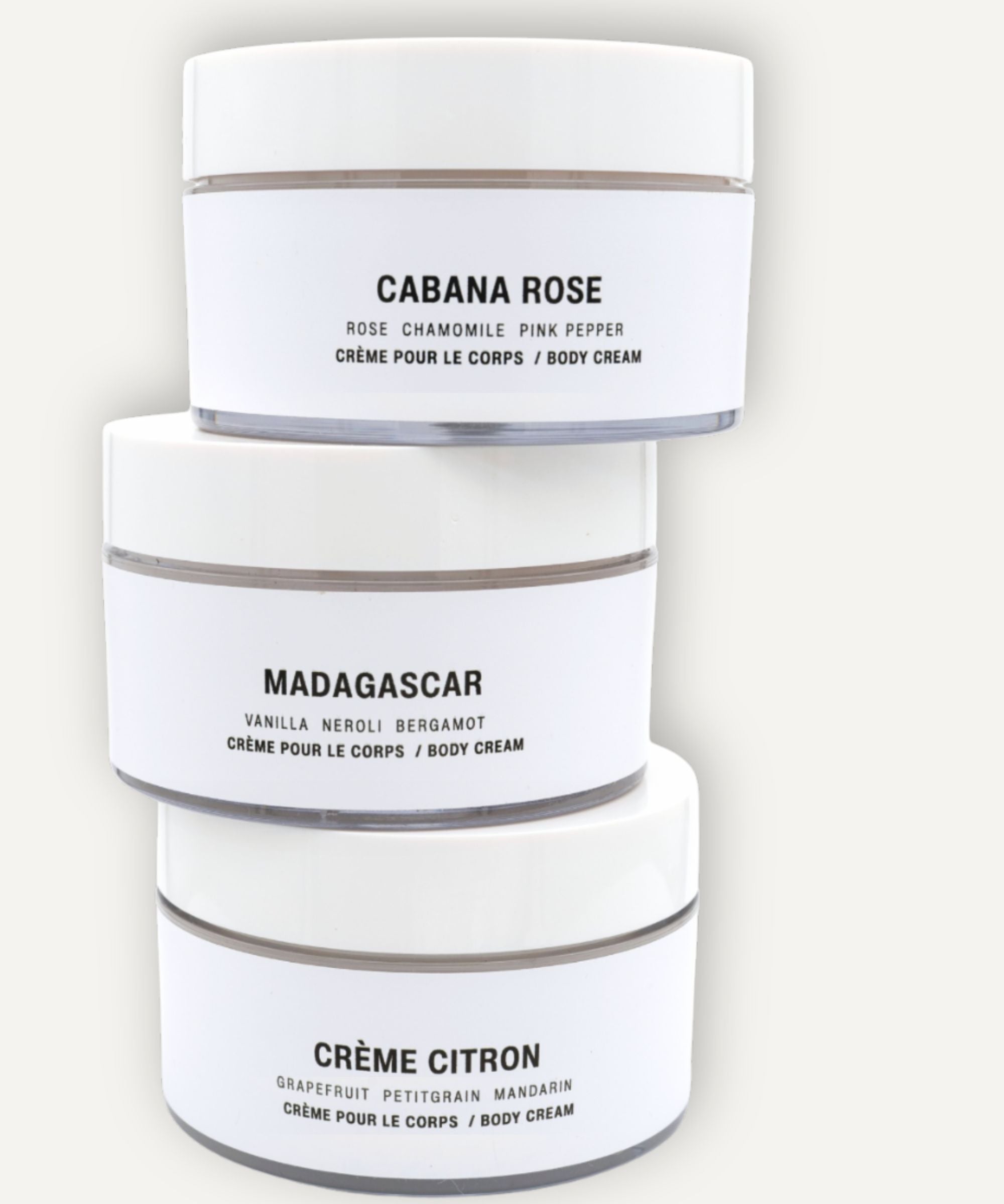 Three cylindrical containers of body cream stacked on a white  bbackground