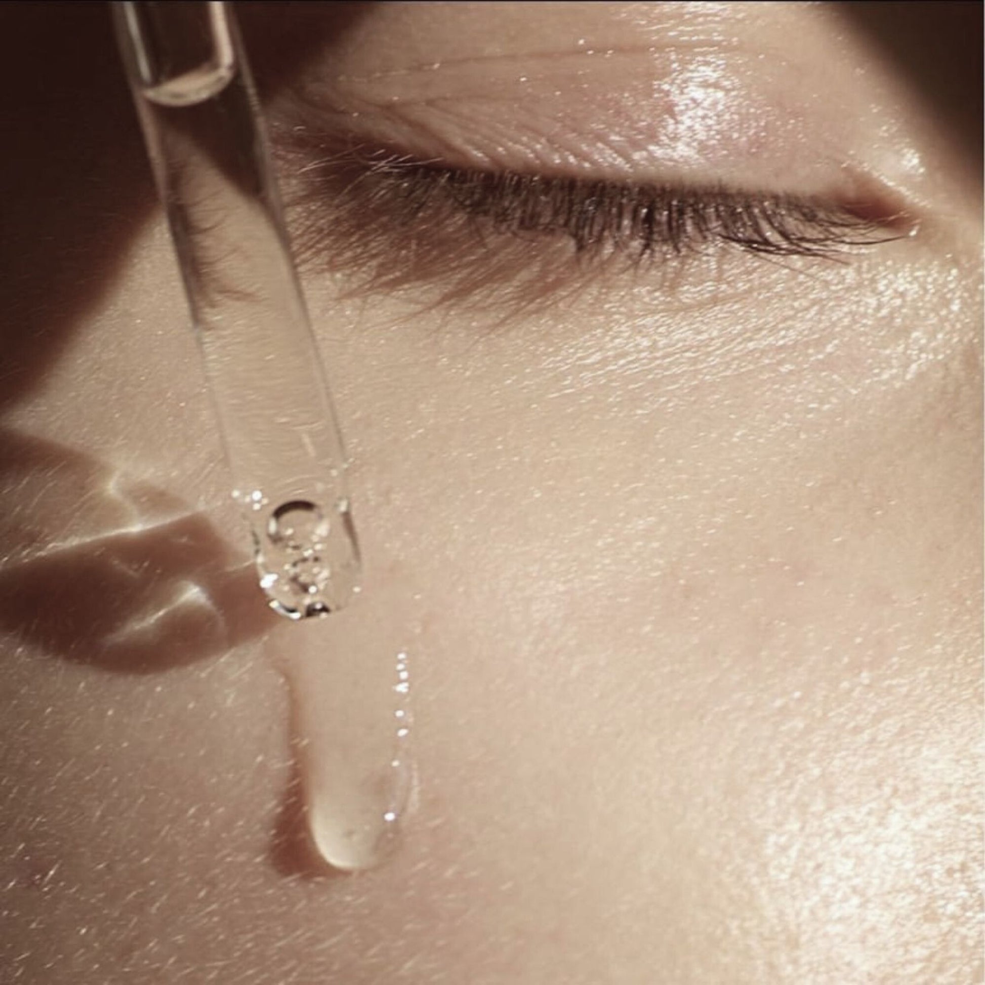 Close-up of a dropper with a drop of liquid being applied to skin.