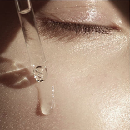 Close-up of a dropper with a drop of liquid being applied to skin.