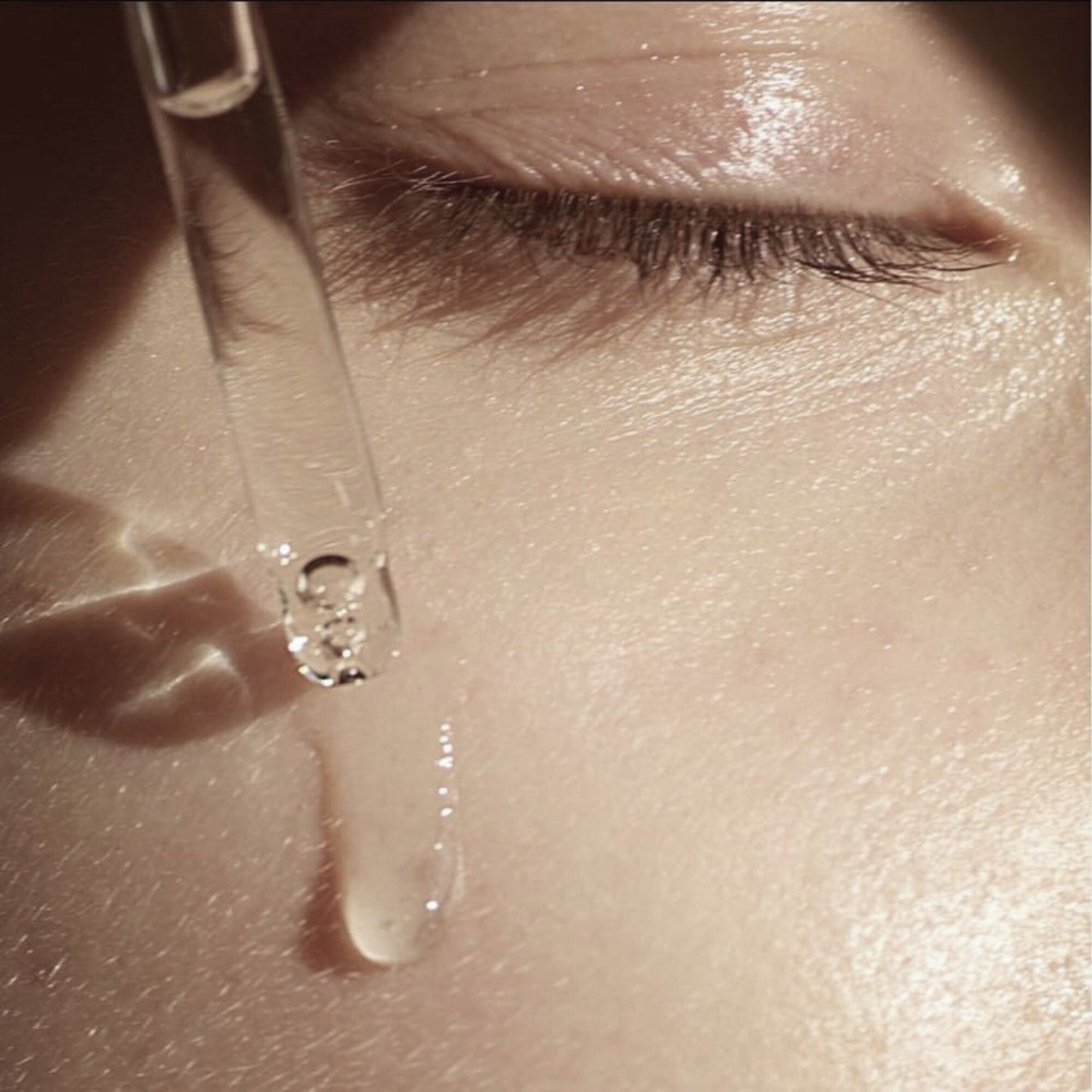 Close-up of a dropper with a drop of liquid being applied to skin.
