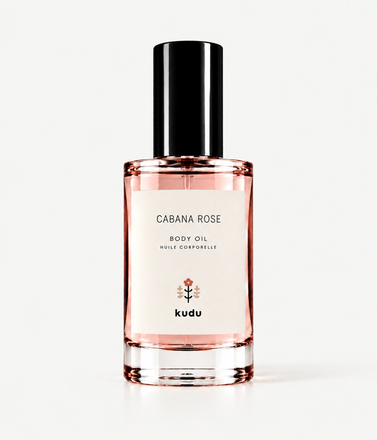 A bottle of Kudu Cabana Rose Body Oil on a clean white background. The clear glass bottle shows the pink rose-colored oil inside, with a white label and a black cap.