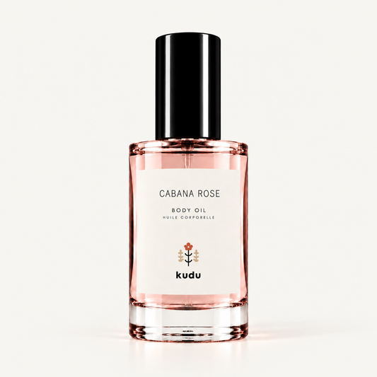 A bottle of Kudu Cabana Rose Body Oil on a clean white background. The clear glass bottle shows the pink rose-colored oil inside, with a white label and a black cap.