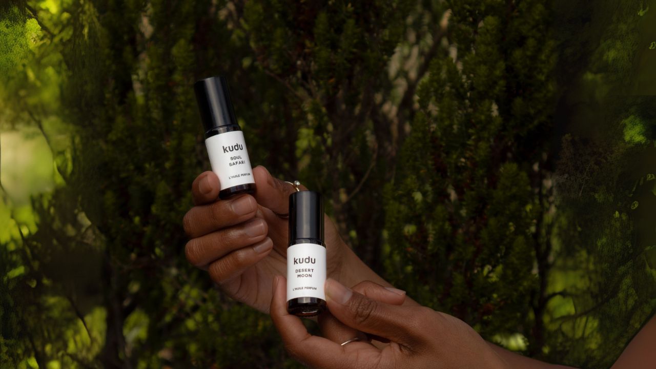 Two bottles of Kudu Cosmetica's product held by a person against a green leafy background